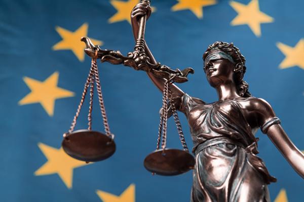 Statue of the blindfolded goddess of justice Themis or Justitia, against an European flag, as a legal concept